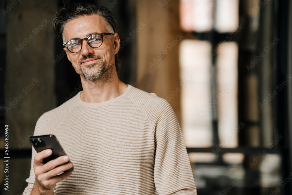 Middle-aged man smiling at camera and holding mobile phone indoors Middle-aged man smiling at camera and holding mobile phone indoors