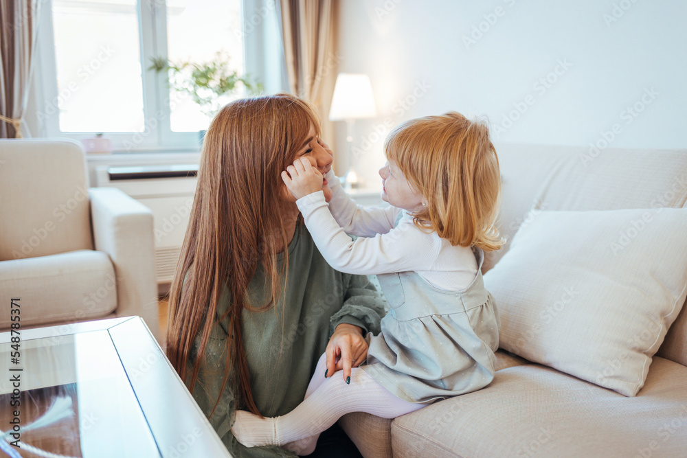 Fototapeta premium Mother and daughter having fun on sofa. Beautiful young woman and her charming little daughter are hugging and smiling. Happy loving family. Mother and her daughter child girl playing and hugging.