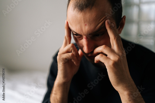 Close-up face of exhausted male sitting alone at home touching head, feeling sad, frustrated, depressed, suffering from headache after quarrel with wife. Frustrated man pondering make difficult choice
