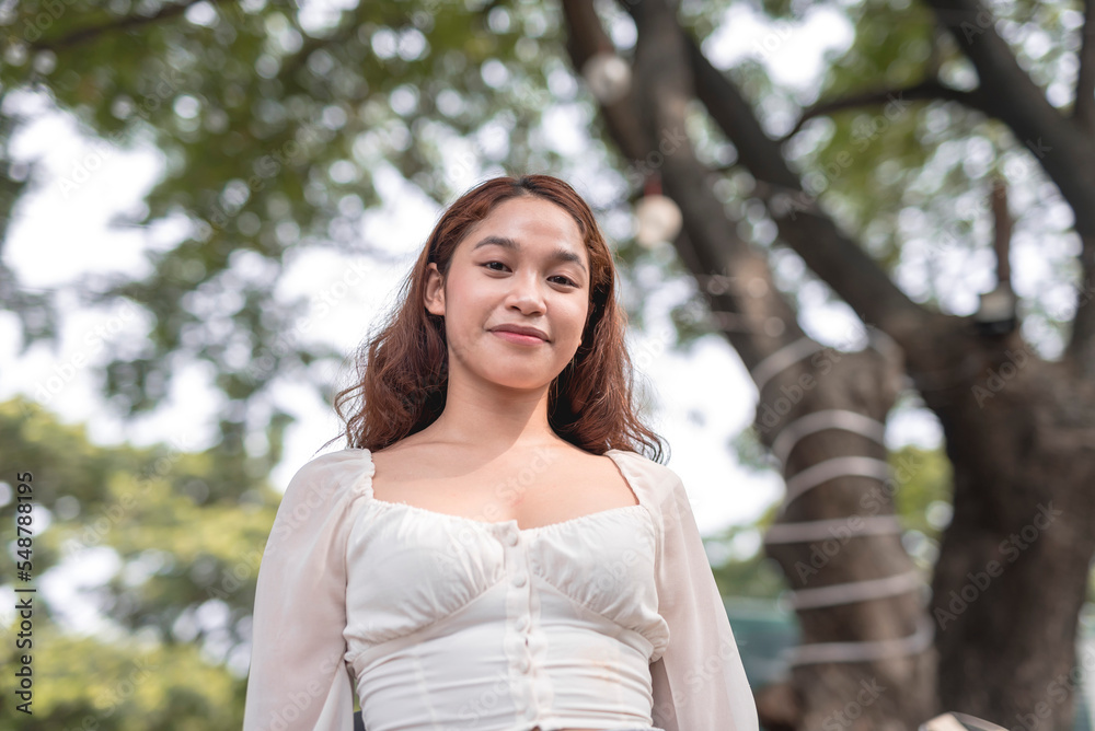A lovely young woman dressed in a trendy white puffed sleeves smiles for the camera on a sunny afternoon outside the park. A lovely young woman dressed in a trendy white puffed sleeves smiles for the camera on a sunny afternoon outside the park.
