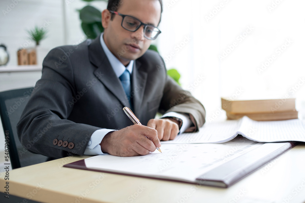 Indian businessman wears business suit marking data report with pen while sitting in the office, selective focus Indian businessman wears business suit marking data report with pen while sitting in the office, selective focus