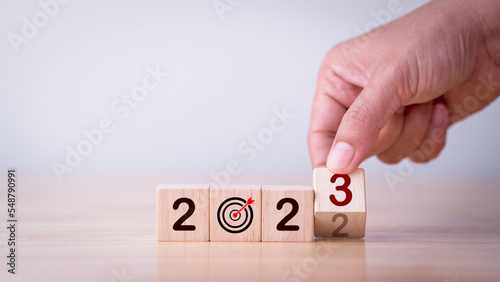 2023 Strategy, Business, Plan, Growth, Investment, Target, Goal, Success, Development, Background Concept. Businessman hand flipping wooden cube block change year 2022 to 2023 with goal, target symbol