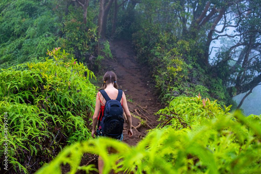 girl with backpack walks among dense green vegetation on kuliouou ridge