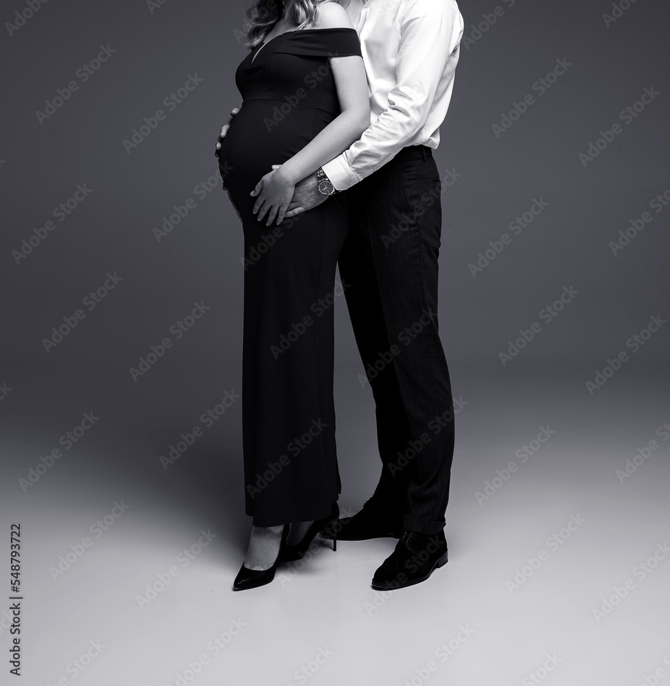 person in a suit, pregnant woman with her husband posing in a studio on a grey background person in a suit, pregnant woman with her husband posing in a studio on a grey background