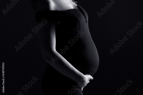 pregnancy woman in black dress on a black background, studio pregnancy shoot