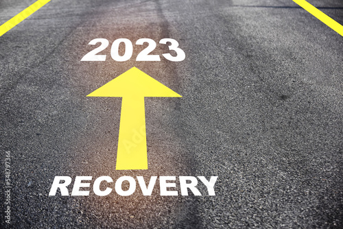 Recovery 2023 with yellow arrow marking on road surface. Business success with direction concept and intelligence future ahead idea