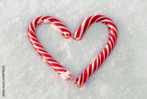 Christmas candy canes as heart on natural white snow backround close-up, top view photo
