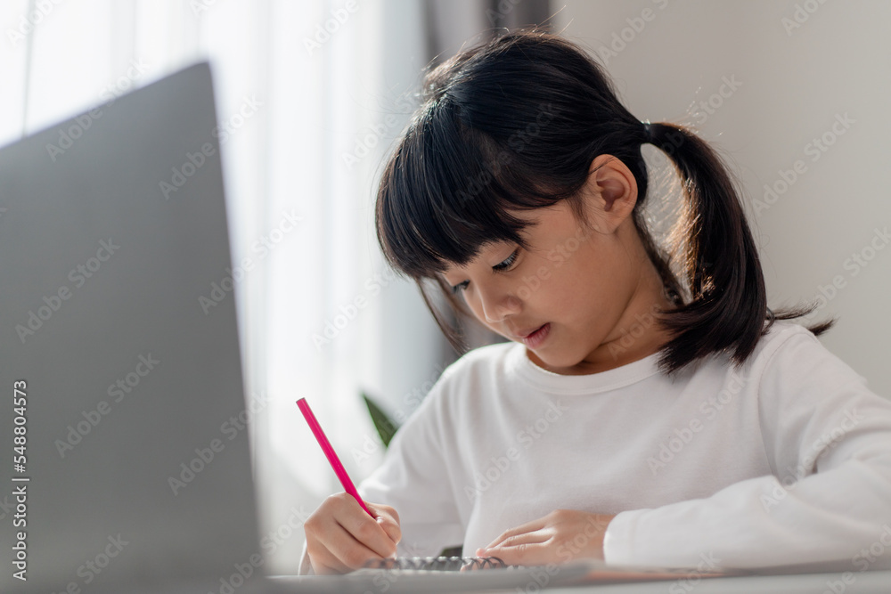 Asian schoolgirl doing her homework with laptop at home. Children use gadgets to study. Education and distance learning for kids. Homeschooling during quarantine. Stay at home Asian schoolgirl doing her homework with laptop at home. Children use gadgets to study. Education and distance learning for kids. Homeschooling during quarantine. Stay at home