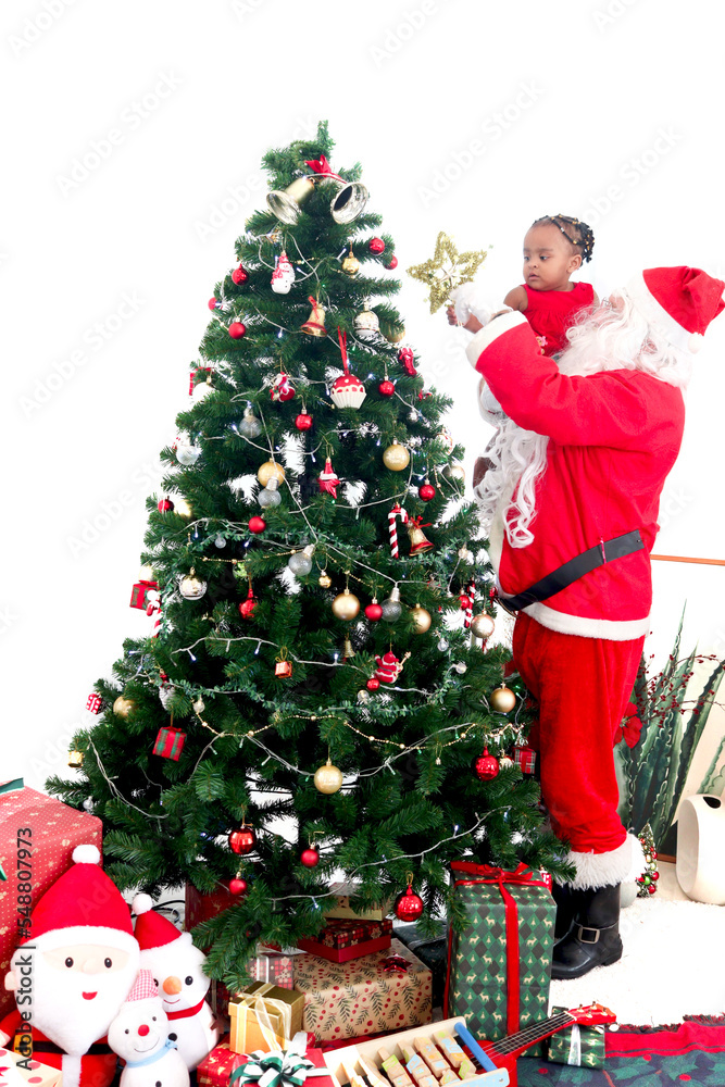Santa Claus holding adorable African American little girl child and helping her to decorate top of Christmas tree with a star, Merry Christmas happy winter holiday celebration