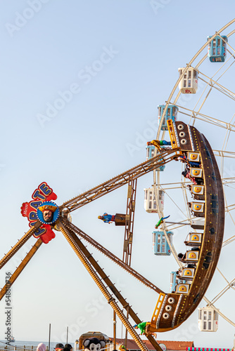 pirate ship and ferris wheel in the amusement park of Sablettes promenade. People riding the ship and having fun in a sunny day with clear blue sky. photo