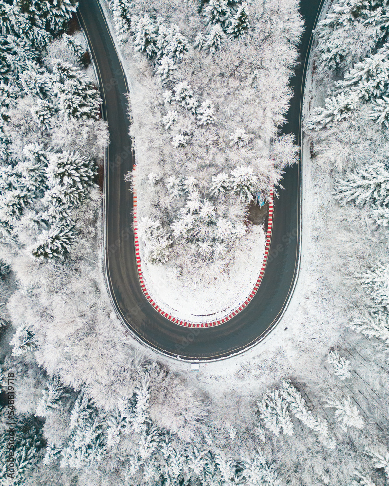 Photo from the drone. Winter landscape. Mountain winding road in a dense snow-covered forest.