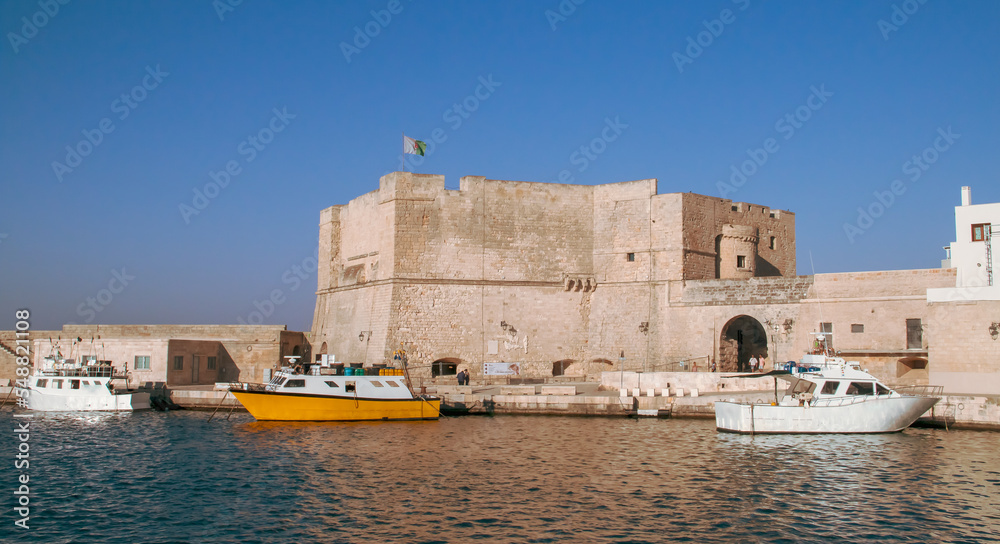 Castillo de Carlos V en el puerto de Monopoli, Italia. Viejo puerto con sus barcos anclados o atracados en el muelle y rodeado de los edificios antiguos de arquitectura medieval.