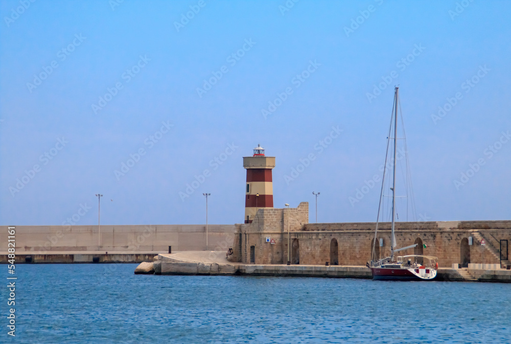 Faro rojo de Monopoli en Italia. Viejo puerto protegido por un muro y rompeolas que protege de los temporales a la flota pesquera y de recreo en el interior del mismo.