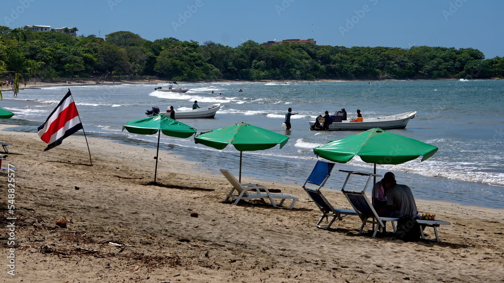 Costa Rican flag by green beach umbrellas on the beach in Tamarindo
