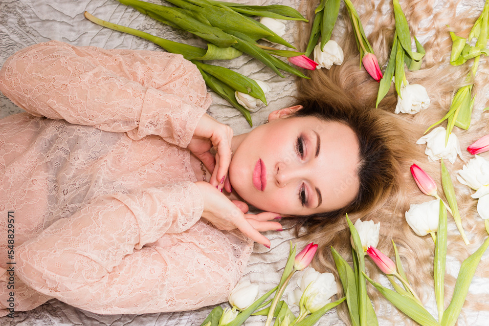 Naklejka premium Portrait of a young woman on a bed with tulips in her hair