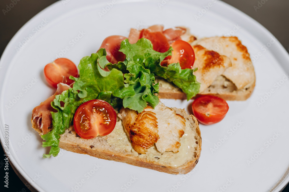 Bruschetta with prosciutto sauce and chicken fillet, garnished with greens and tomatoes.