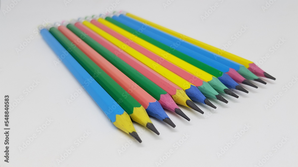 A selection of blue, yellow, pink and green hexagon shaped pencils with coloured erasers lined up next to each other.