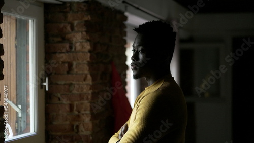 African man standing by window thinking about life. Concerned worried emotion © Marco