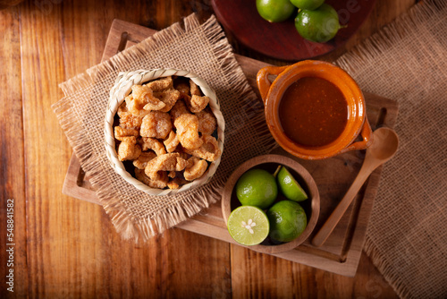 Chicharrones. Deep fried pork rinds, crispy pork skin pieces, traditional mexican ingredient or snack served with lemon juice and red hot chili sauce.