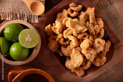 Chicharrones. Deep fried pork rinds, crispy pork skin pieces, traditional mexican ingredient or snack served with lemon juice and red hot chili sauce. photo