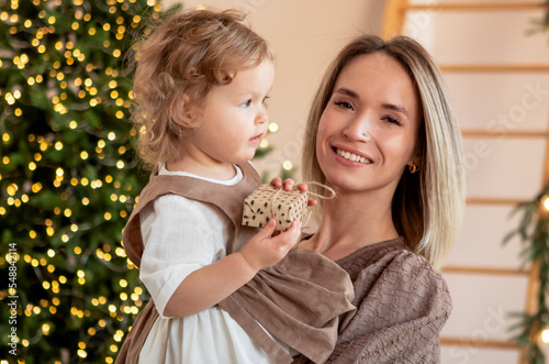 young mother with a girl by the Christmas tree celebrates the new year