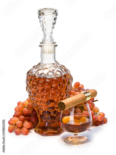 A decanter and a glass filled with cognac, a cigar and a bunch of grapes