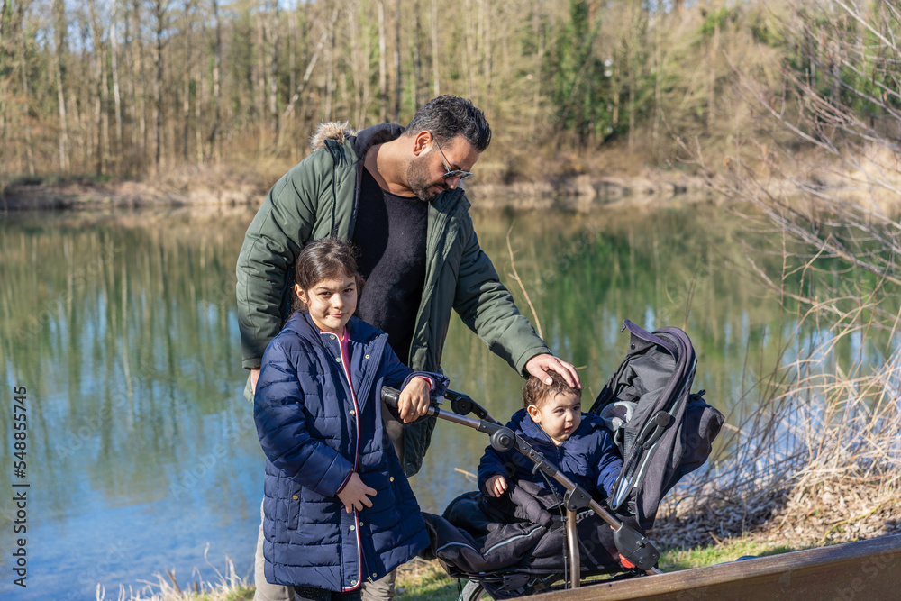 Father with stroller and two children walking along the Aare river in springtime. Father with stroller and two children walking along the Aare river in springtime.