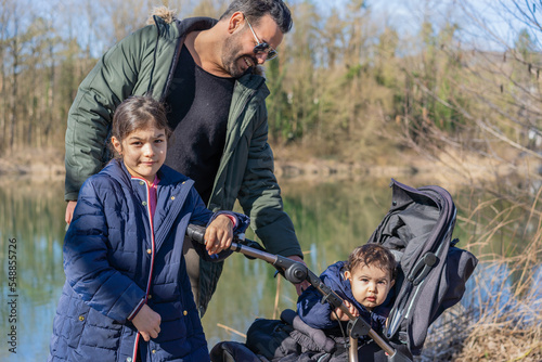 Close-up of father with stroller and two children walking along the Aare river in springtime.