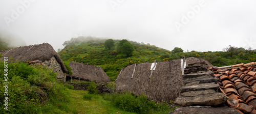 Vistas panorámicas del techo de paja de una casa tradicional en la Braña de Pornacal, de Asturias, en un día de niebla blanca y césped verde, España, 2021 photo