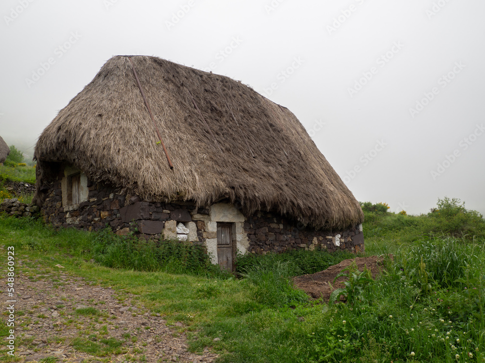 Vistas de una casa tiípica en la Braña de Pornacal, de Asturias, con techo de paja en verano, un día de niebla blanca y césped verde, España, 2021