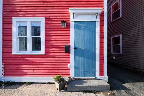 A bright red wooden exterior wall of a country style house. The wall is made of red narrow wood clapboard cape cod siding. There s a small wooden door  a double pane glass window  and a black mailbox.
