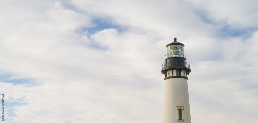 The high tower of a white lighthouse against the background of a sky covered with white fluffy clouds. Travel destinations, excursions, travel, beauty of nature. There are no people in the photo.