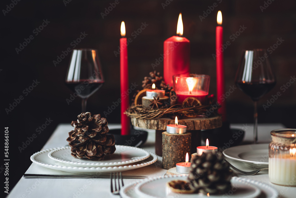 Rustic table decor for Christmas or New Year family dinner. Centrepiece with red candle, dry orange, cone, cinnamon, anise. Zero waste eco-friendly home. Cozy atmosphere, dark background. Close up