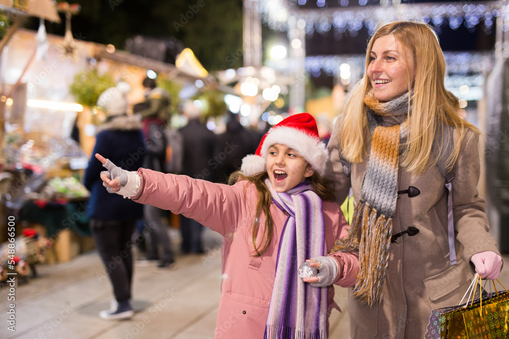 Smiling woman with tweenage daughter pointing to something while choosing decorations on traditional Christmas market