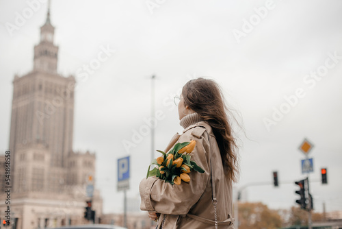 A young girl in glasses with flowers against the background of the Palace of Culture in Warsaw. A pretty girl in glasses with flowers walks in Warsaw.