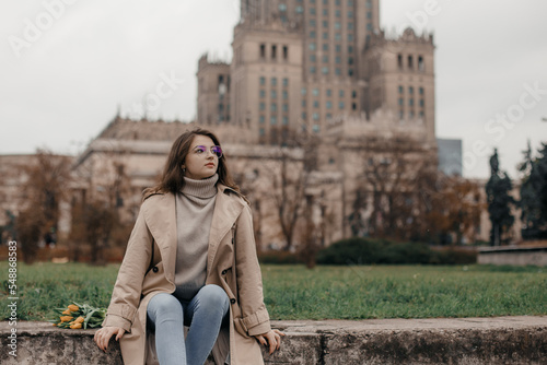 A walk near the Palace of Culture. A girl with yellow tulips against the background of the Palace of Culture in Poland. A pretty girl in glasses with flowers walks in Europe city.