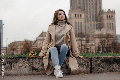 A walk near the Palace of Culture. A girl with yellow tulips against the background of the Palace of Culture in Poland. A pretty girl in glasses with flowers walks in Europe city.