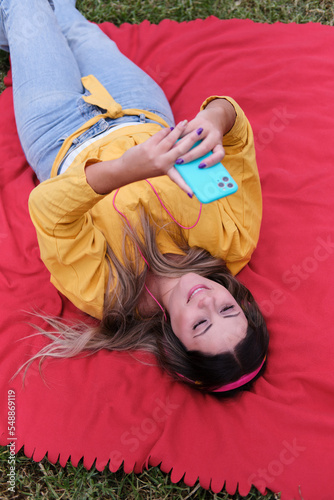 Girl listening to music while looking at her mobile phone lying on the grass