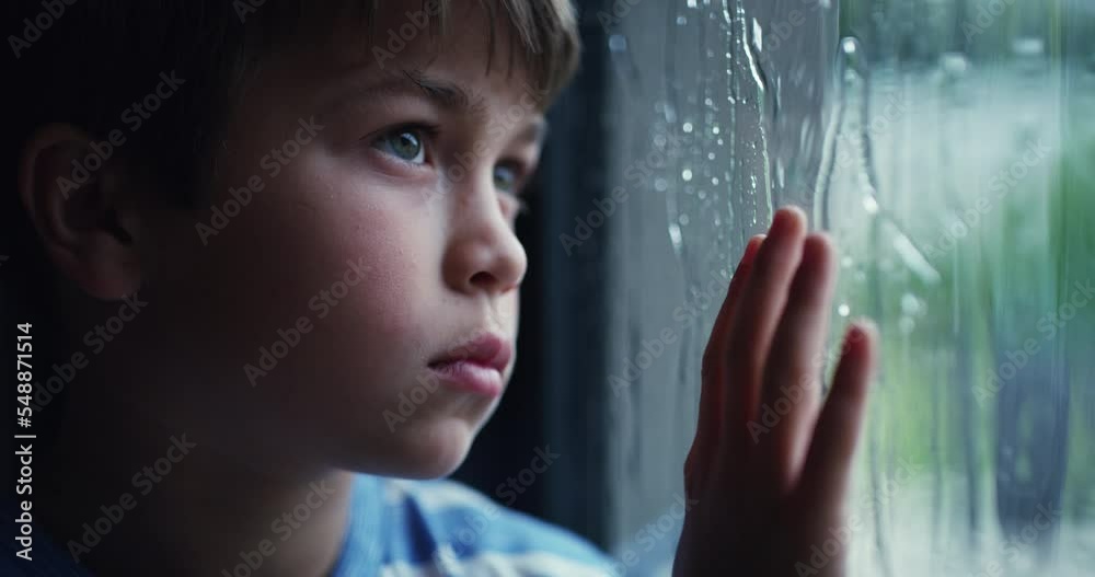 Children, bored and raining with a sad boy standing by the window, looking or thinking about wet winter weather. Kids, glass and depression with a male child feeling sadness alone in his home