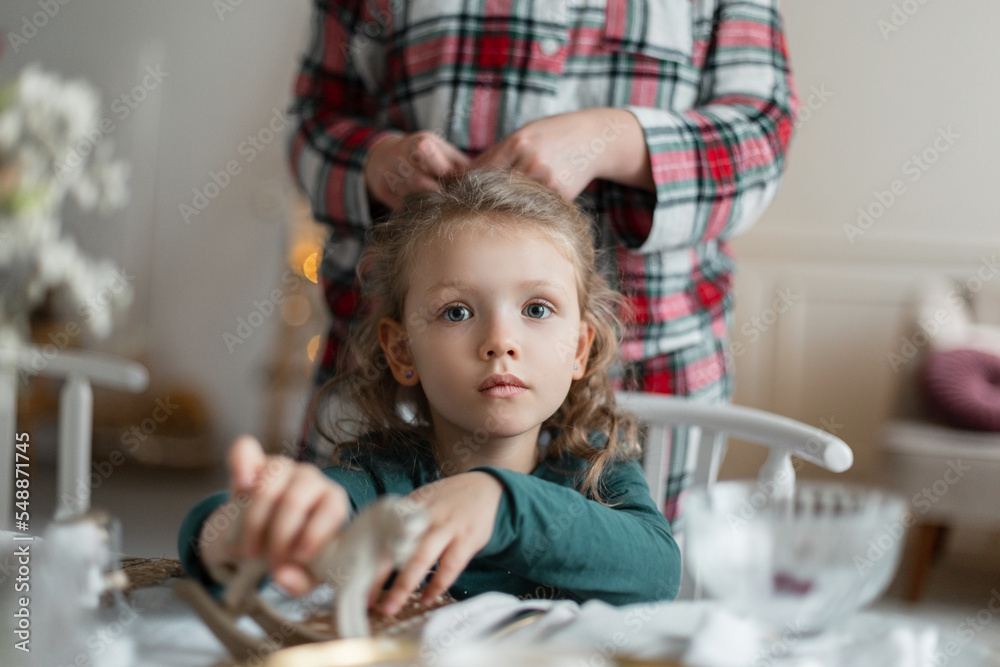 Beautiful baby girl sits at the festive table and mom does her hair on Christmas Eve Beautiful baby girl sits at the festive table and mom does her hair on Christmas Eve