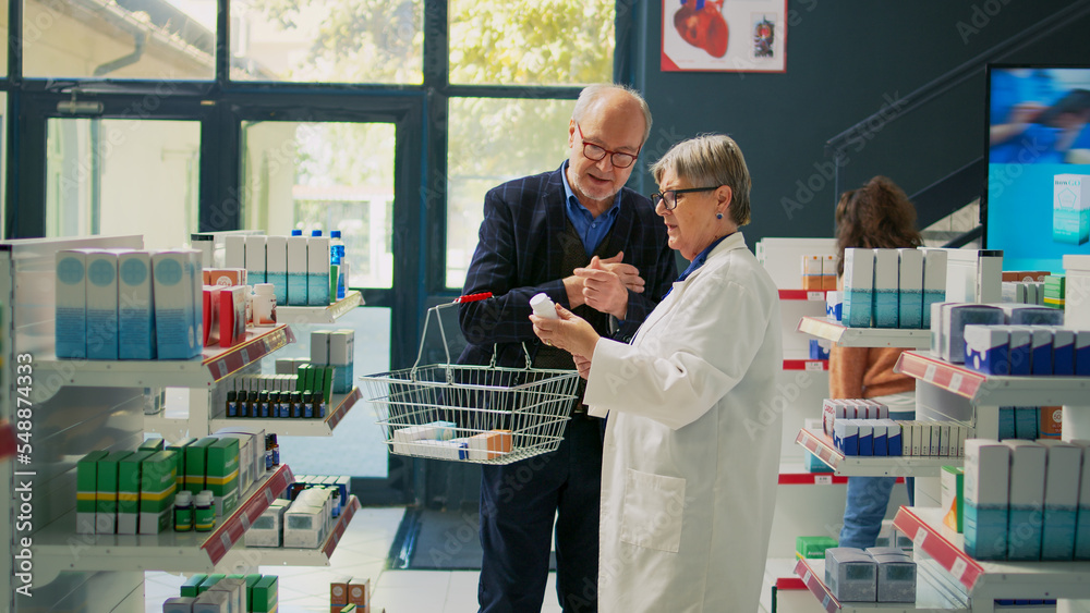 Obraz premium Elderly man showing prescription paper to pharmacist, asking for help with buying treatment and medicaments. Senior client talking to drugstore worker about vitamins and pills on shelves.
