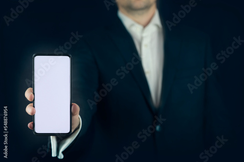Fototapeta Naklejka Na Ścianę i Meble -  A man (business) holding cell phone (mobile phone). Free (blank) white space to use. Telly screen (mockup). All with dark blue background. Ideally for business presentations. 