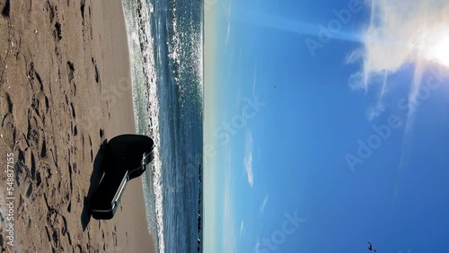 Guitar case on the sandy beach. Vertical mobile phone video orientation. Beautiful sunny day at the seaside, blue sky and sparkling water. A quitarist left his guitar on sand photo