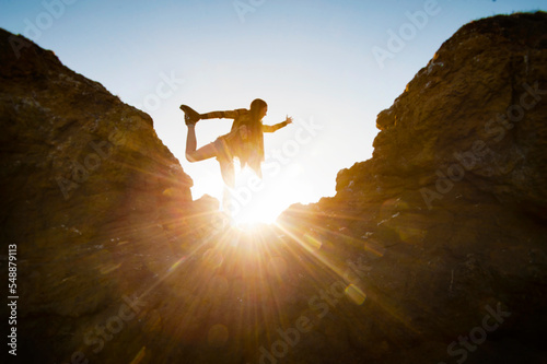Higher Self. Silhouette of a young woman in dancer's yoga pose on a mountain with the sun flaring behind her. 