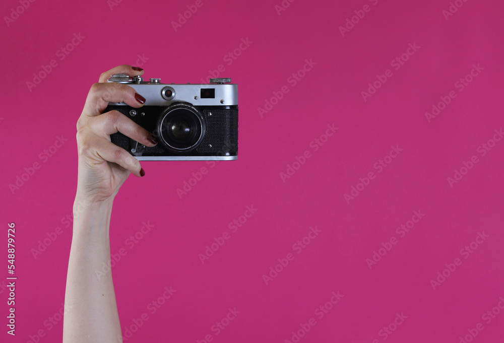 retro camera in a female hand on a pink background