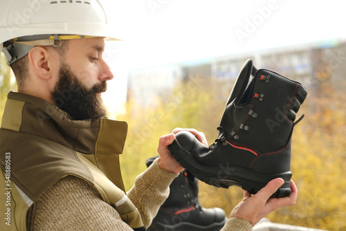 black work boots made of leather with reinforced cape, high top in hands of young bearded man, builder in uniform, concept of highest product quality, special shoes for different professions photo