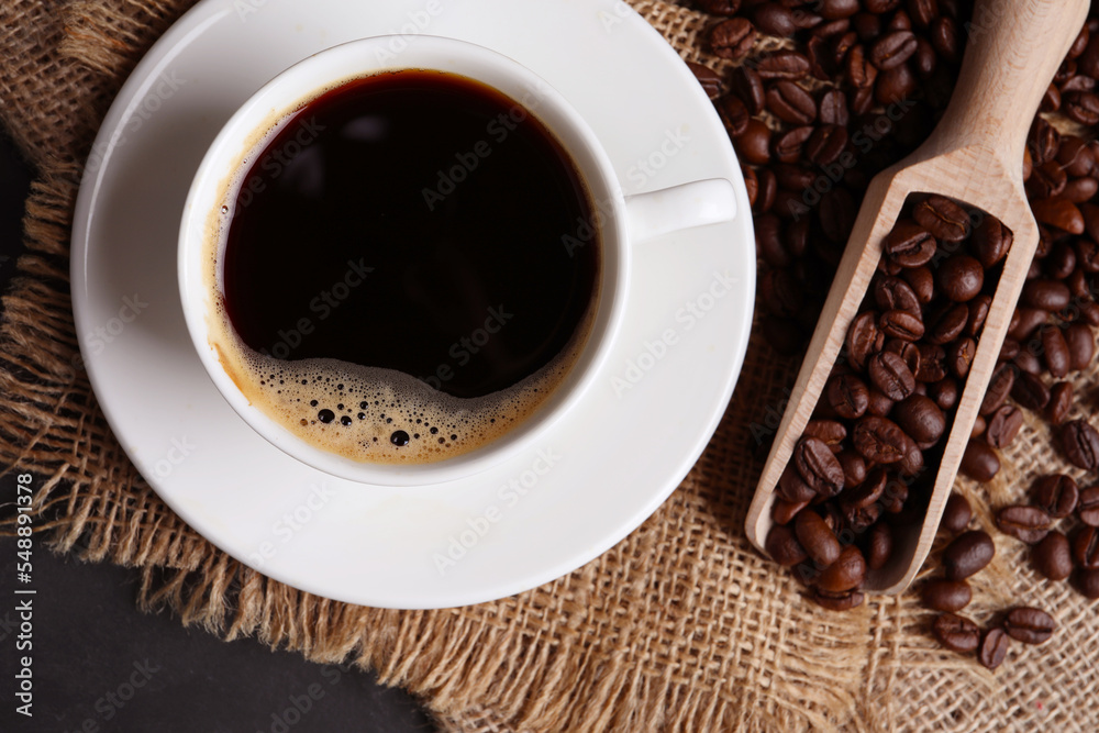 Fototapeta premium Cup of hot aromatic coffee and scoop with roasted beans on black table, top view