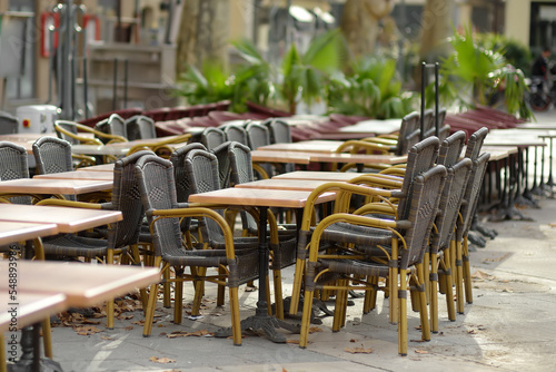 Fototapeta Naklejka Na Ścianę i Meble -  An empty outdoor cafe in a European city on an autumn day. Chairs and tables are stacked. Fallen leaves are lying on the ground. Restaurant closed. End of the season.