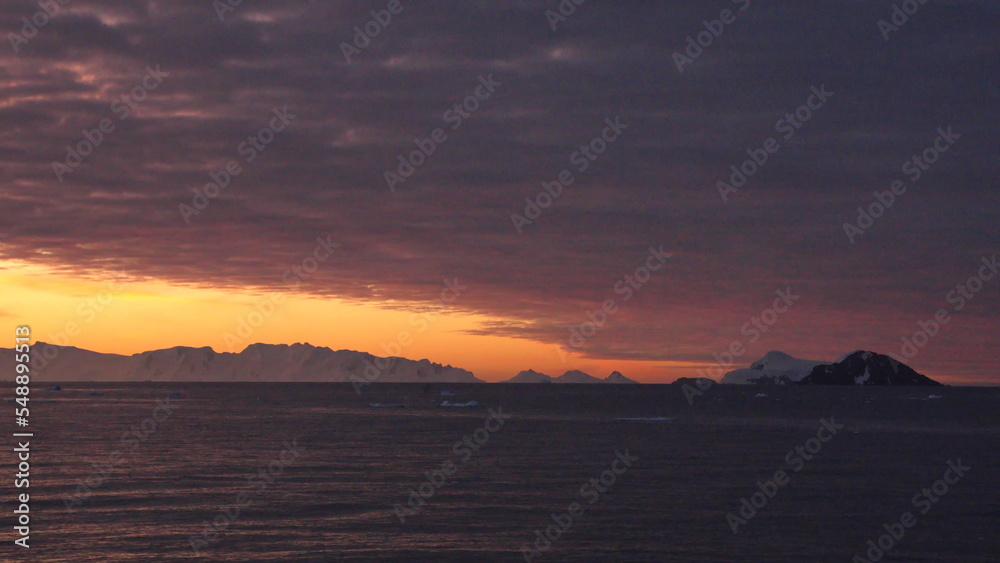 Pink clouds in an orange sky, with mountains and icebergs in silhouette, at Cierva Cove, Antarctica, at sunset