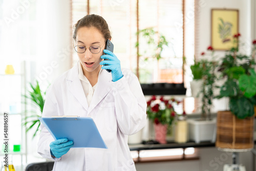 portrait young smiling confident female doctor or scientist, healthcare professional talking on phone, giving consultation. Plant Laboratory background. © Wongsakorn